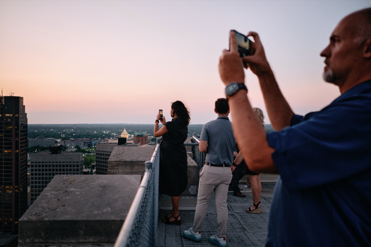 Guests photographing the sunset skyline from the rooftop, the State Capitol dome in the distance