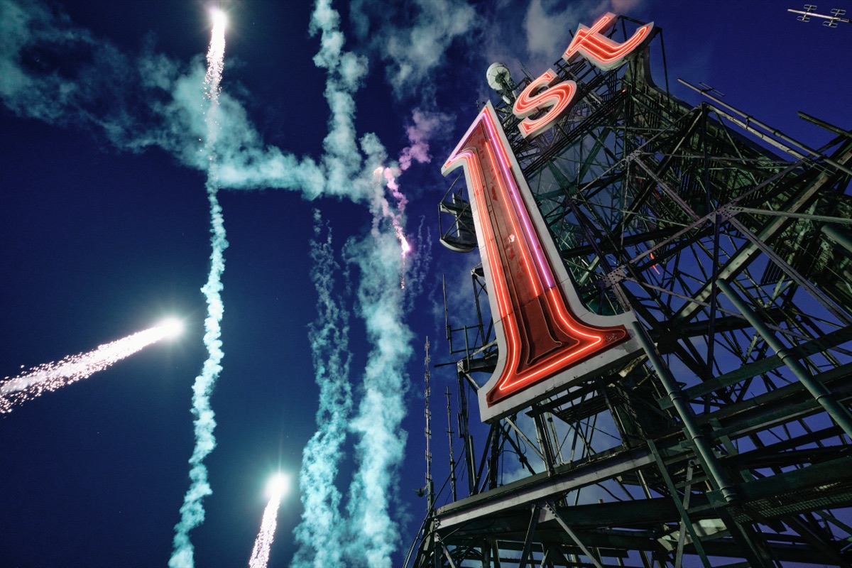 Fireworks streaking into a deep blue dusk sky beside the relit 1st sign